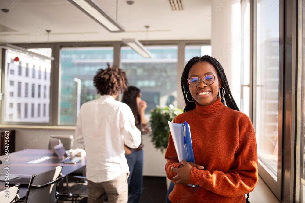 Black girl in office in foreground is looking at camera