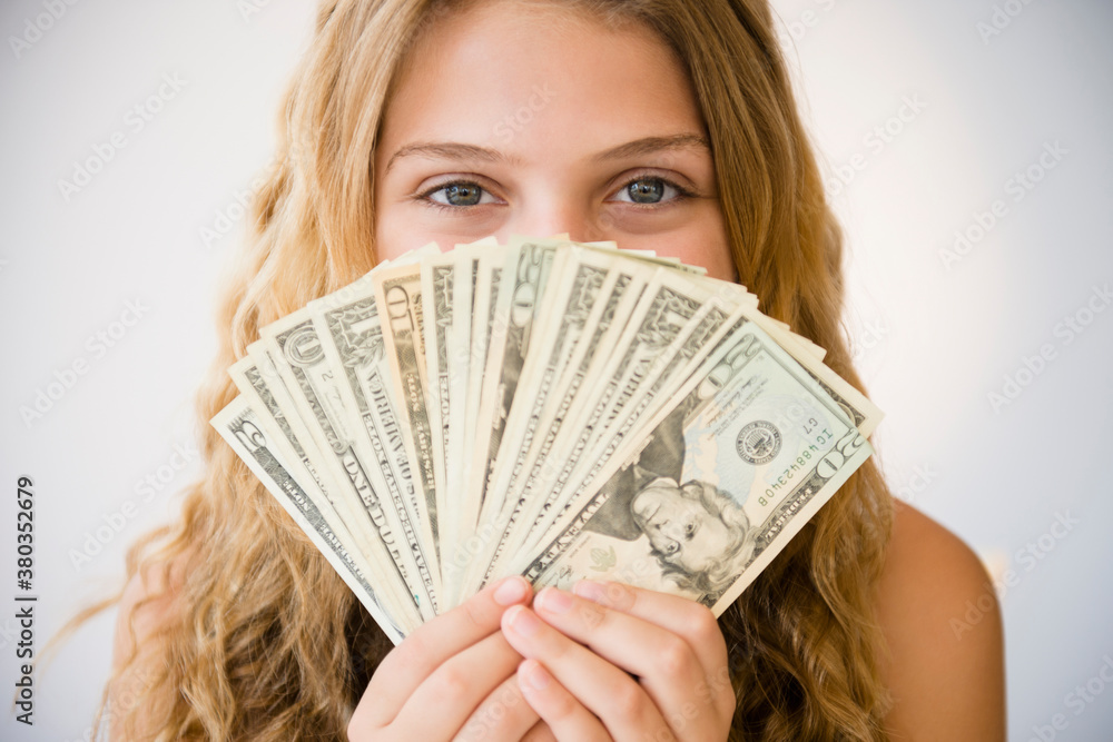 Girl (12-13) holding money fan against her face